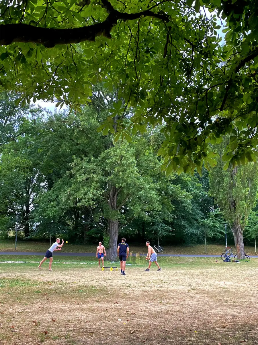 Grupo de jóvenes jugando roundnet en el césped del Seepark junto al lago Flückiger, deporte popular en los parques de Friburgo