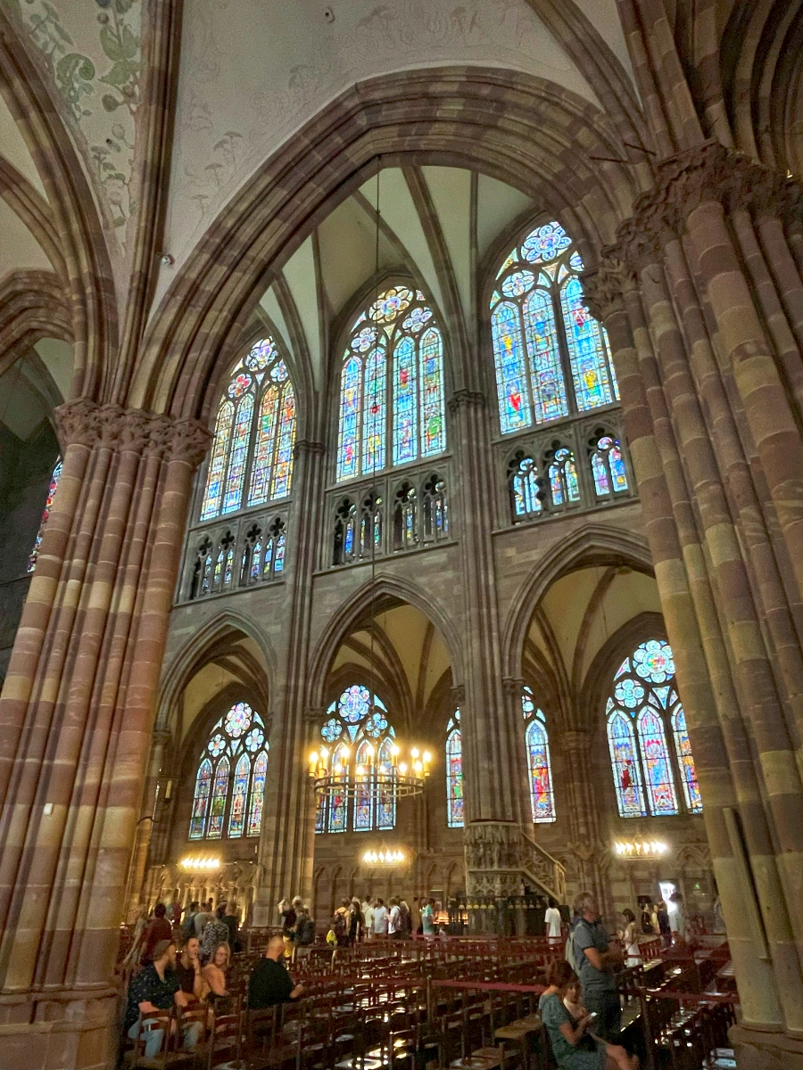 Interior de la Catedral de Estrasburgo con arcos góticos y vitrales iluminados sobre las naves laterales