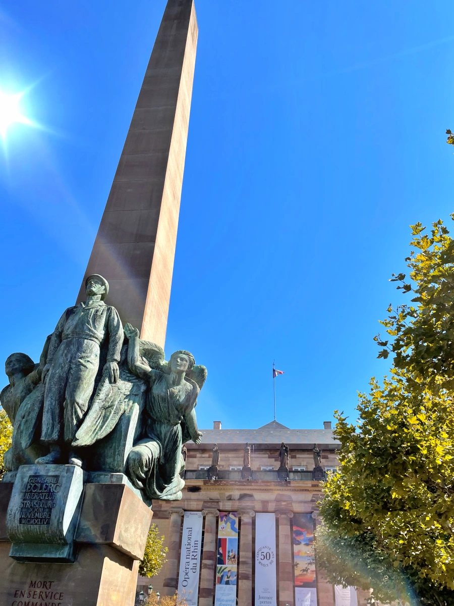 Monumento al Maréchal Leclerc en forma de obelisco con esculturas de bronce y la Ópera Nacional del Rin al fondo en Place Broglie, Estrasburgo