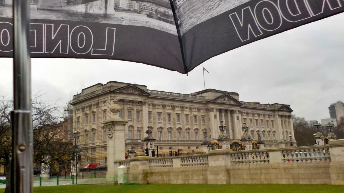 Buckingham Palace de Londres visto desde el exterior en un día lluvioso, con un paraguas decorado con imágenes de la ciudad en primer plano