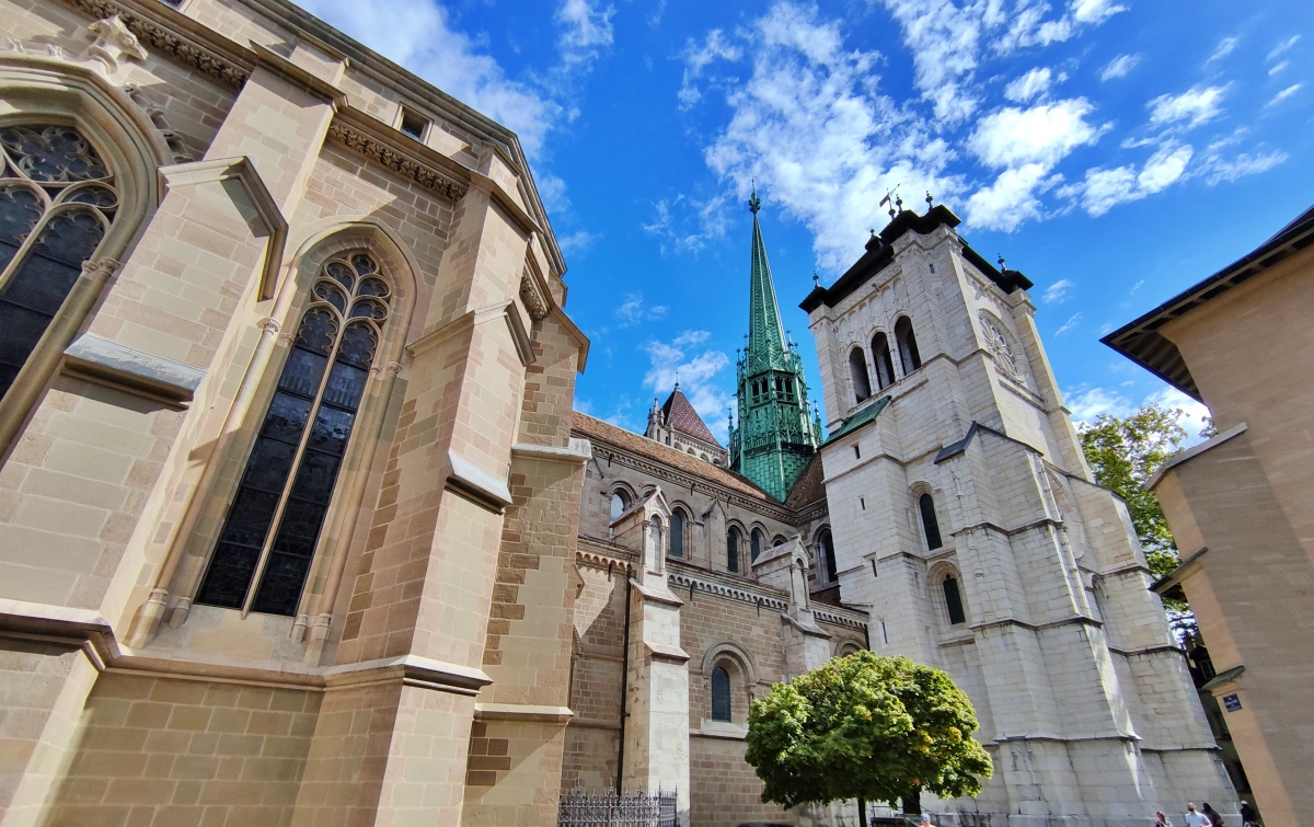 Vista lateral de la Catedral de San Pedro de Ginebra desde la Place du Bourg-de-Four, destacando la torre gótica y la fachada de piedra bajo cielo azul
