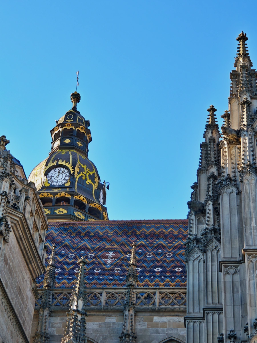 Primer plano del tejado de azulejos policromados y la torre del reloj con detalles dorados de la Catedral de Santa Isabel en Košice, Eslovaquia, ejemplo destacado de arquitectura gótica.