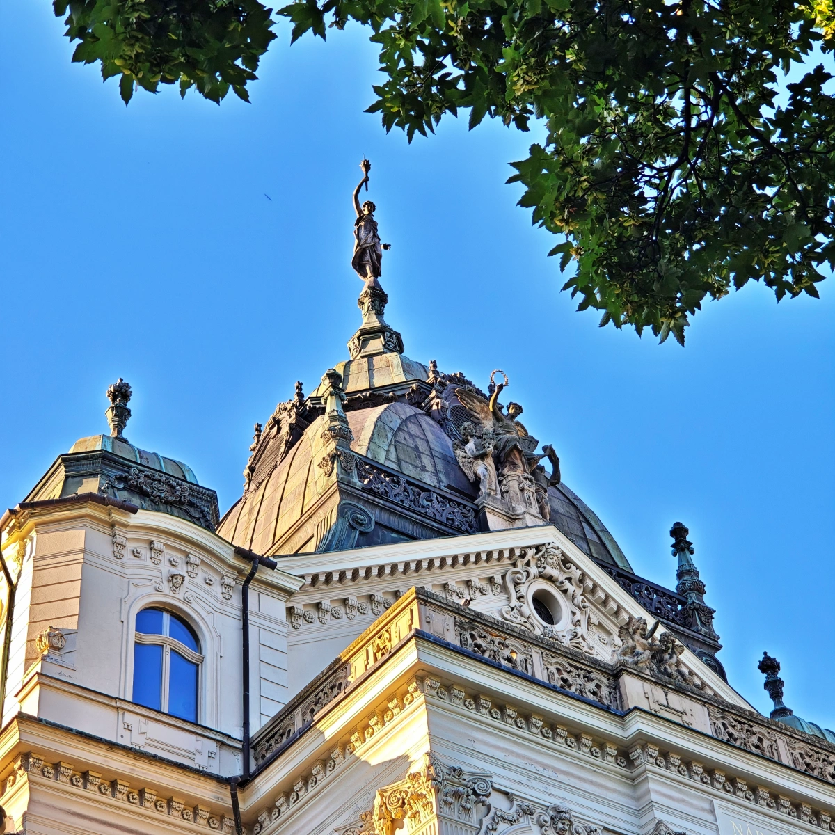 Primer plano del tejado del Teatro Estatal de Košice, Eslovaquia, mostrando la cúpula central, esculturas ornamentales y detalles arquitectónicos bajo un cielo azul intenso.