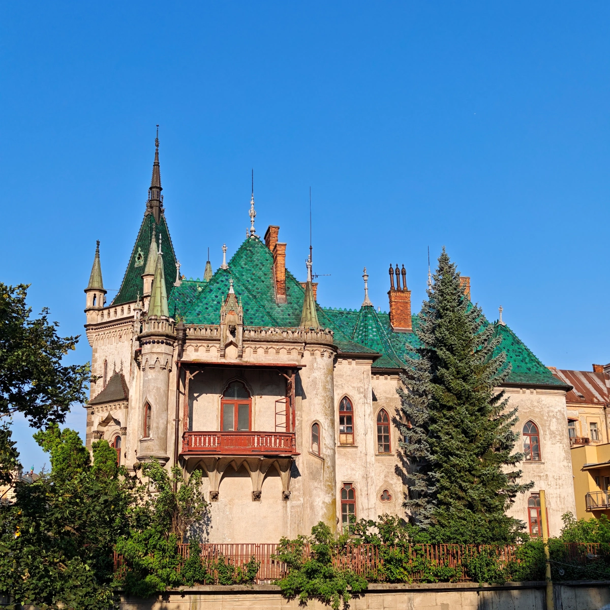 Fachada del Palacio Jakab en Košice, Eslovaquia, con techo verde y torres neogóticas bajo un cielo azul claro.