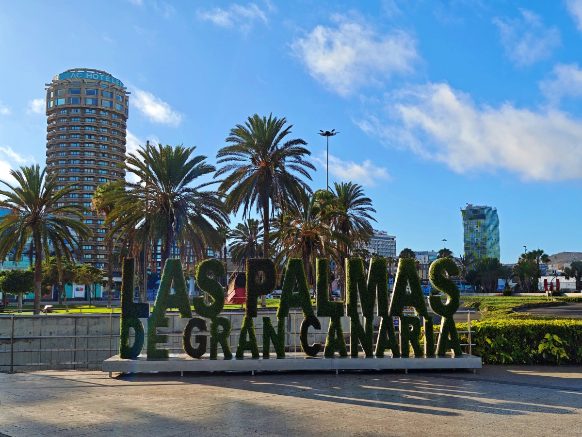 Cartel vegetal de "Las Palmas de Gran Canaria" en el Parque Santa Catalina, rodeado de palmeras y edificios emblemáticos como la torre Woermann.