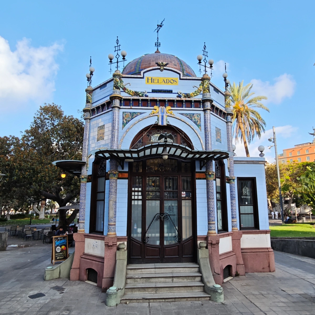 Vista frontal del kiosco modernista en el Parque San Telmo decorado con azulejos, cúpula de cerámica y carteles de helados.