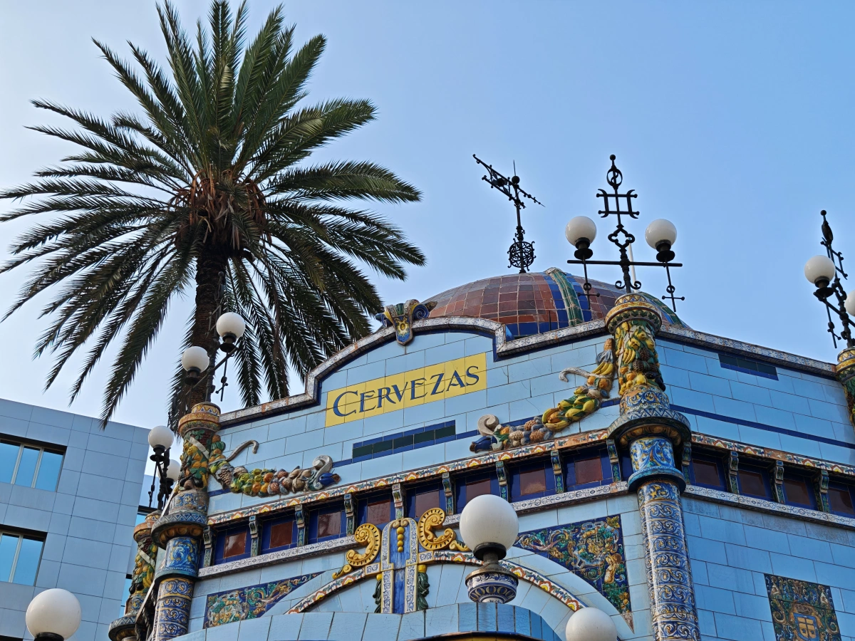 Detalle arquitectónico del kiosco modernista de San Telmo, destacando el cartel de cervezas, la cúpula y esculturas con palmera al fondo.