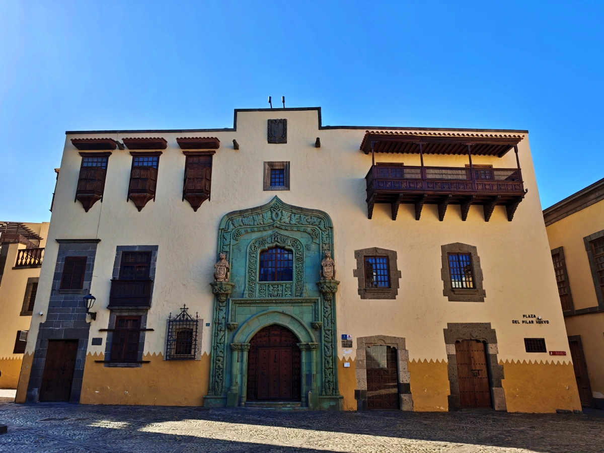 Imagen panorámica de la Casa de Colón con balcones de madera, ventanas de piedra y su característico portal, ubicada en la Plaza del Pilar Nuevo en el barrio de Vegueta.