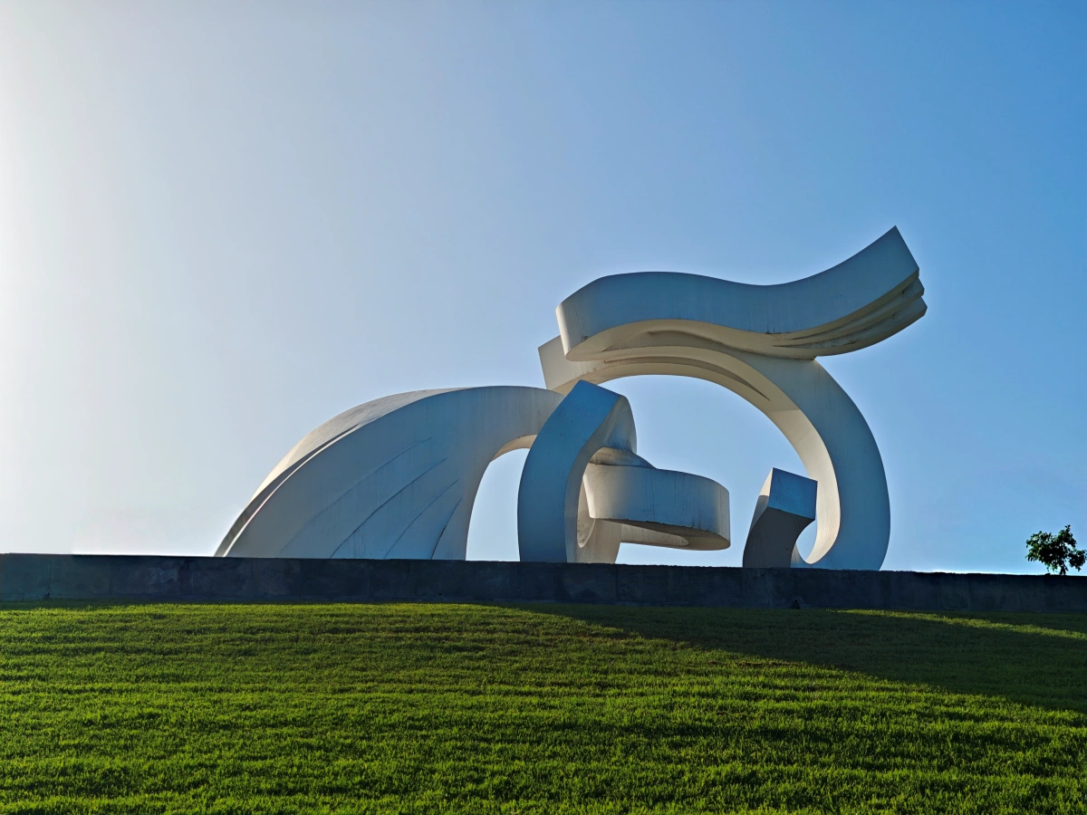 Escultura contemporánea Lady Harimaguada en Las Palmas de Gran Canaria sobre césped, con silueta curvilínea y cielo azul de fondo.