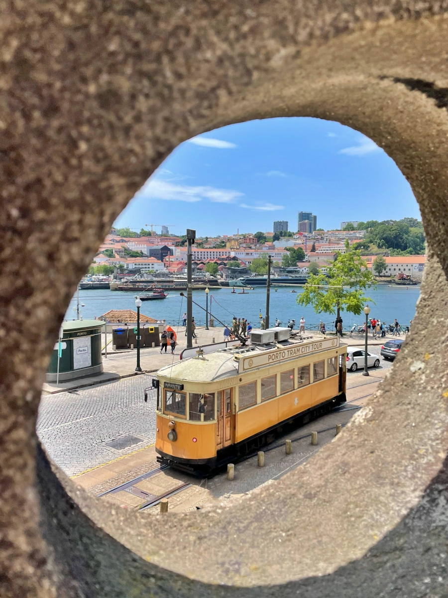 Tranvía turístico amarillo visto a través de un agujero en barandilla con el río Duero al fondo