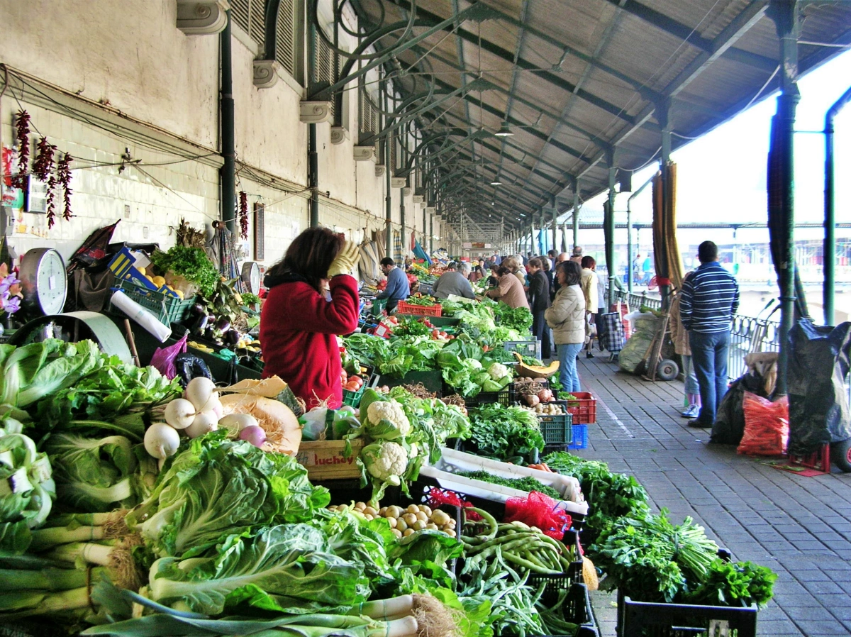 Vendedora entre montones de verduras frescas en pasillo cubierto del Mercado do Bolhão