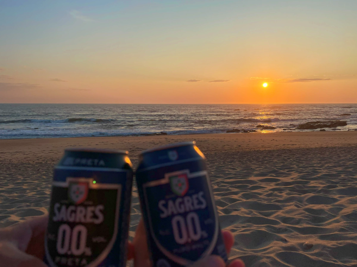 Dos latas de cerveza Sagres 0.0% en primer plano con puesta de sol dorada sobre el mar al fondo