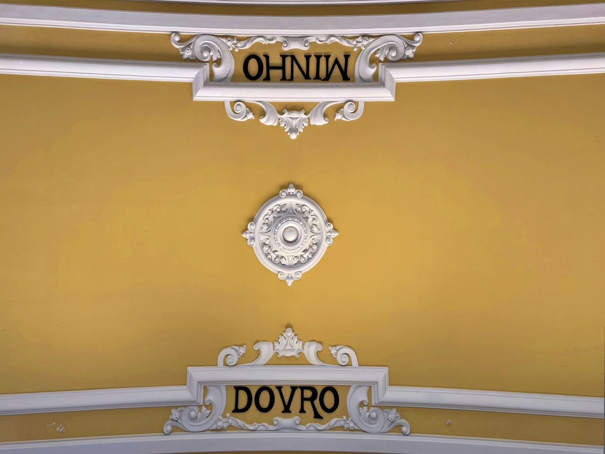 Detalle de las molduras blancas y los nombres “MINHO” y “DOVRO” en el techo amarillo de São Bento