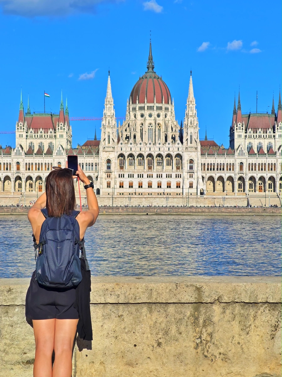 Turista fotografiando el Parlamento de Budapest desde la ribera del río Danubio en un día soleado