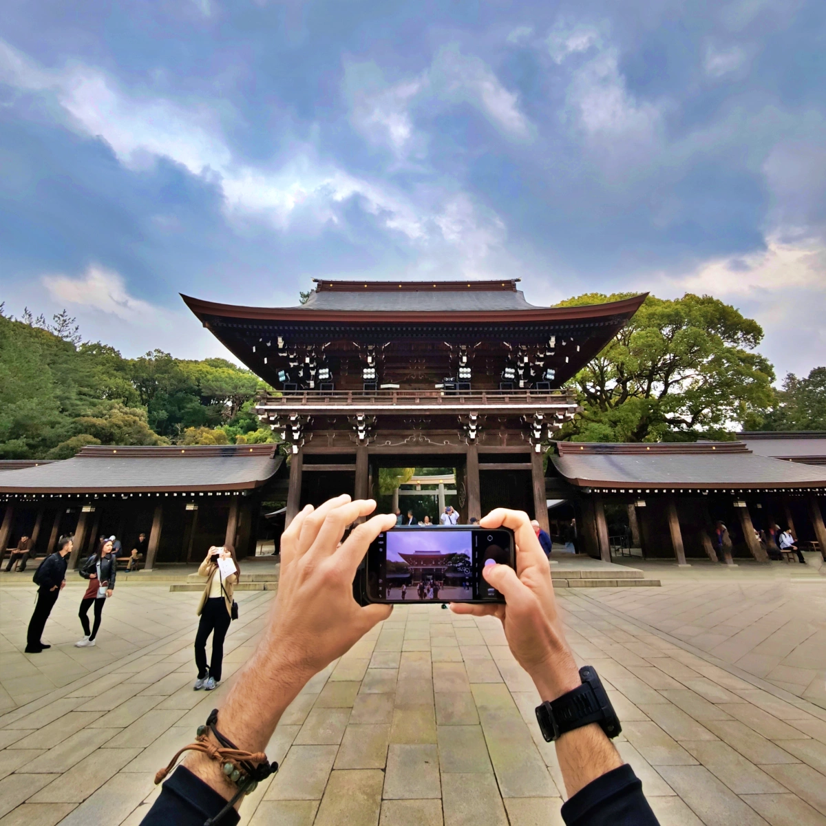 Manos haciendo una foto con el móvil al santuario Meiji Jingu en Tokio bajo cielo nublado