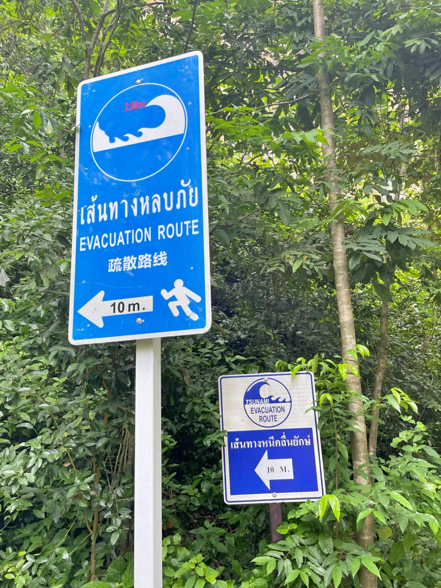Cartel azul de evacuación por tsunami en inglés, tailandés y chino en entorno selvático