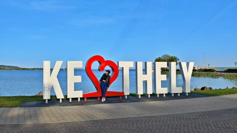 Letrero monumental “KESZTHELY” con corazón rojo, lago Balaton de fondo y persona posando