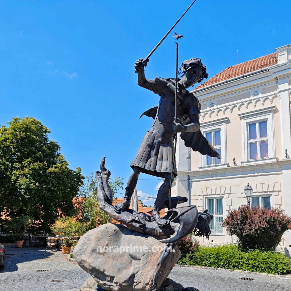 Estatua de San Miguel Arcángel representada con armadura y espada, situada frente a la histórica Torre del Fuego en Veszprém, Hungría.