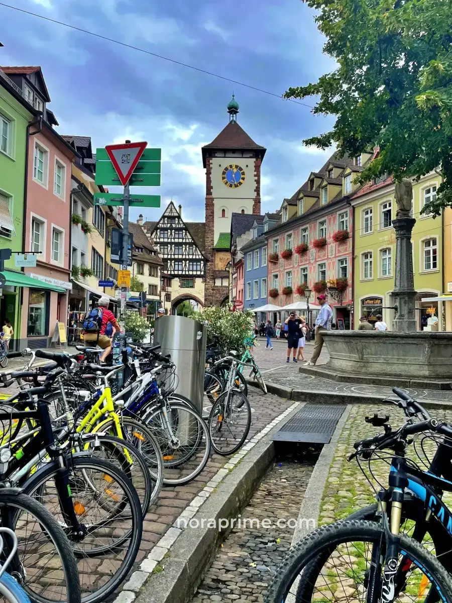 Puerta medieval Schwabentor en Friburgo con Bächle (canal de agua) en primer plano y bicicletas aparcadas, vista desde Oberlindenbrunnen
