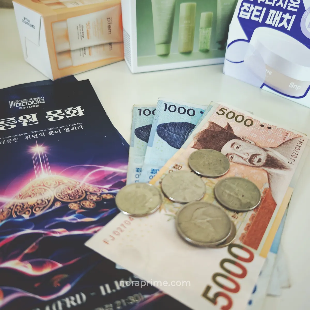 Billetes y monedas de won surcoreano (₩1.000 y ₩5.000) junto a productos de cosmética coreana y un folleto, representando presupuesto de viaje y compras de skincare en Corea del Sur