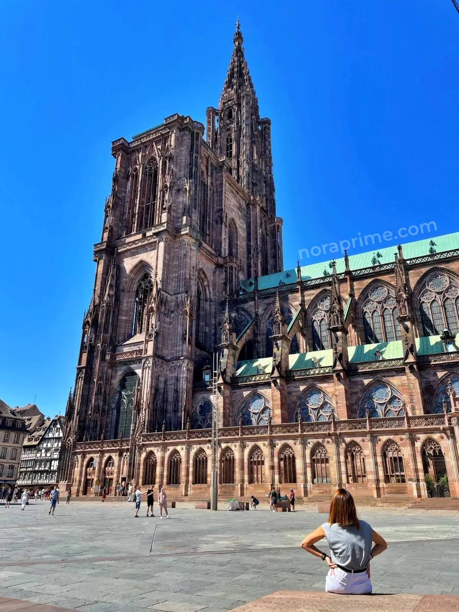 Vista de la torre principal y fachada lateral de la Catedral de Estrasburgo con turistas en la plaza