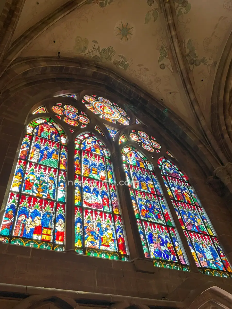 Vidriera lateral de la Catedral de Estrasburgo con escenas bíblicas y colores vivos en el interior gótico