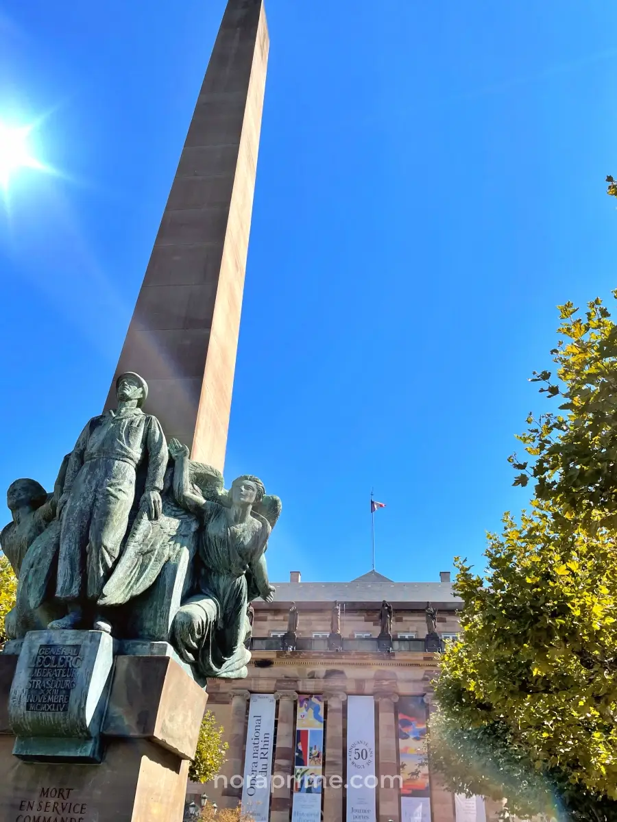 Monumento al Maréchal Leclerc en forma de obelisco con esculturas de bronce y la Ópera Nacional del Rin al fondo en Place Broglie, Estrasburgo