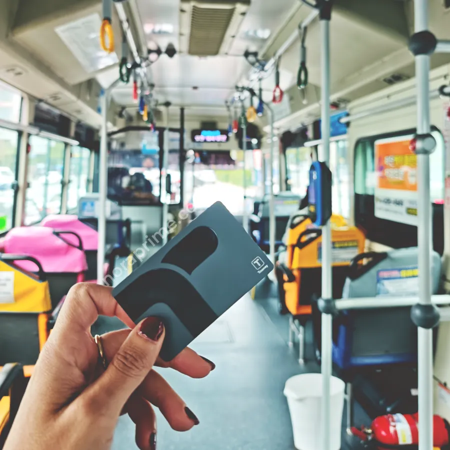 Mano sosteniendo una tarjeta T-money dentro de un autobús urbano en Corea del Sur, con asientos y barras de sujeción al fondo, lista para pagar el billete con pago sin contacto.