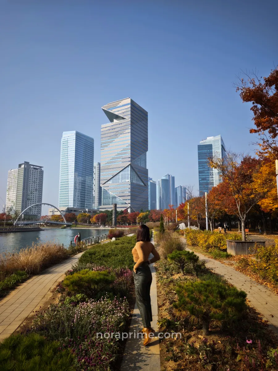 Viajera paseando por Songdo Central Park en Incheon con la G Tower y otros rascacielos al fondo en otoño