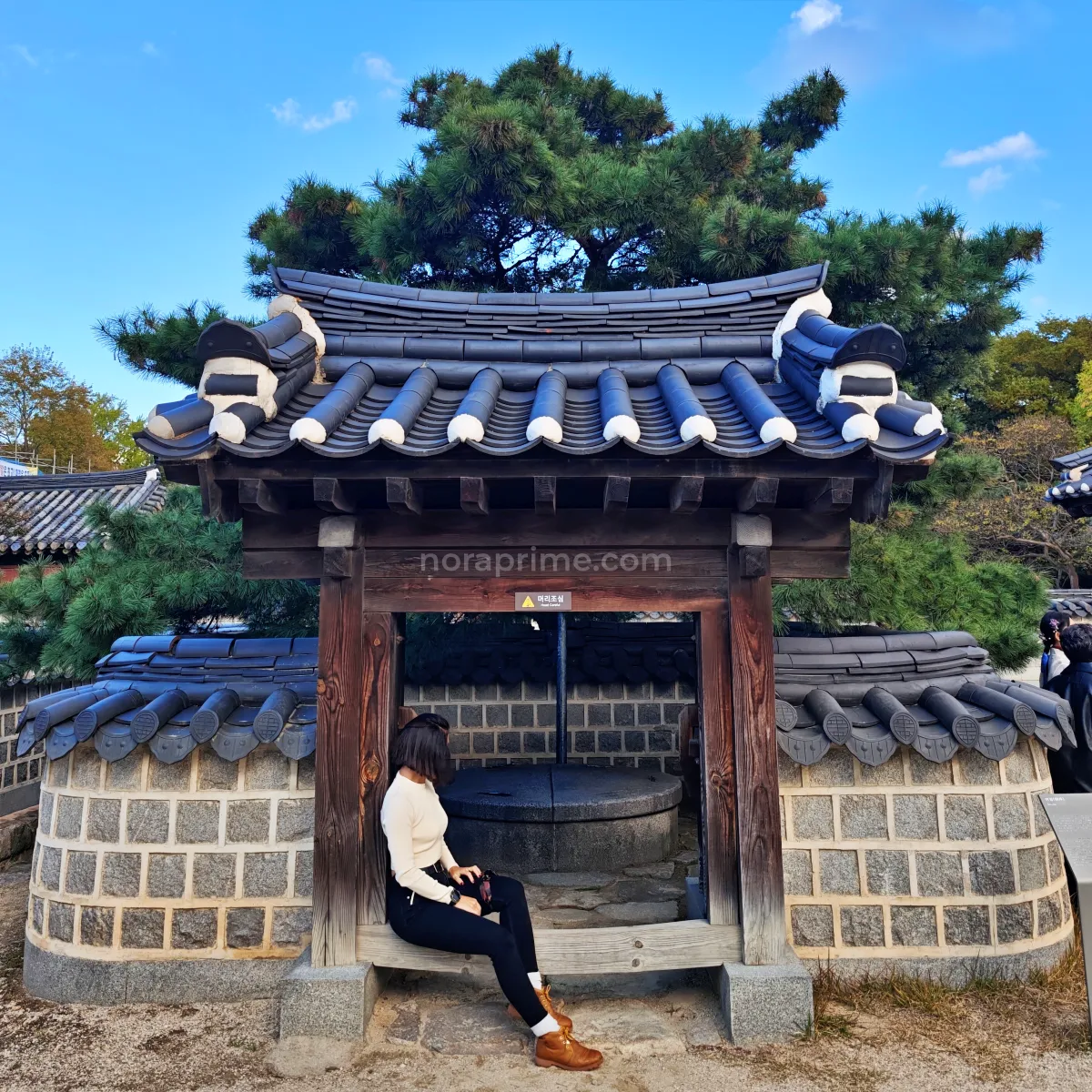 Viajera sentada junto a un pozo tradicional cubierto por un pequeño tejado en Jeonju Hanok Village Corea del Sur