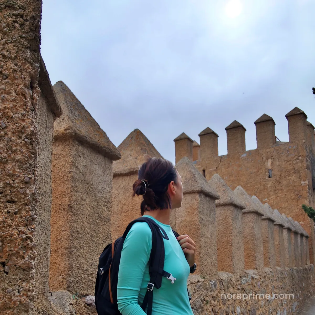 Mujer con mochila caminando junto a las murallas de piedra del Santuario de Sant Salvador en Artà, Mallorca, uno de los pueblos más bonitos de la isla.