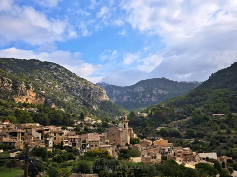 Vista general del pueblo de Valldemossa en Mallorca, con tejados de teja, campanario y montañas de la Serra de Tramuntana rodeando el valle.