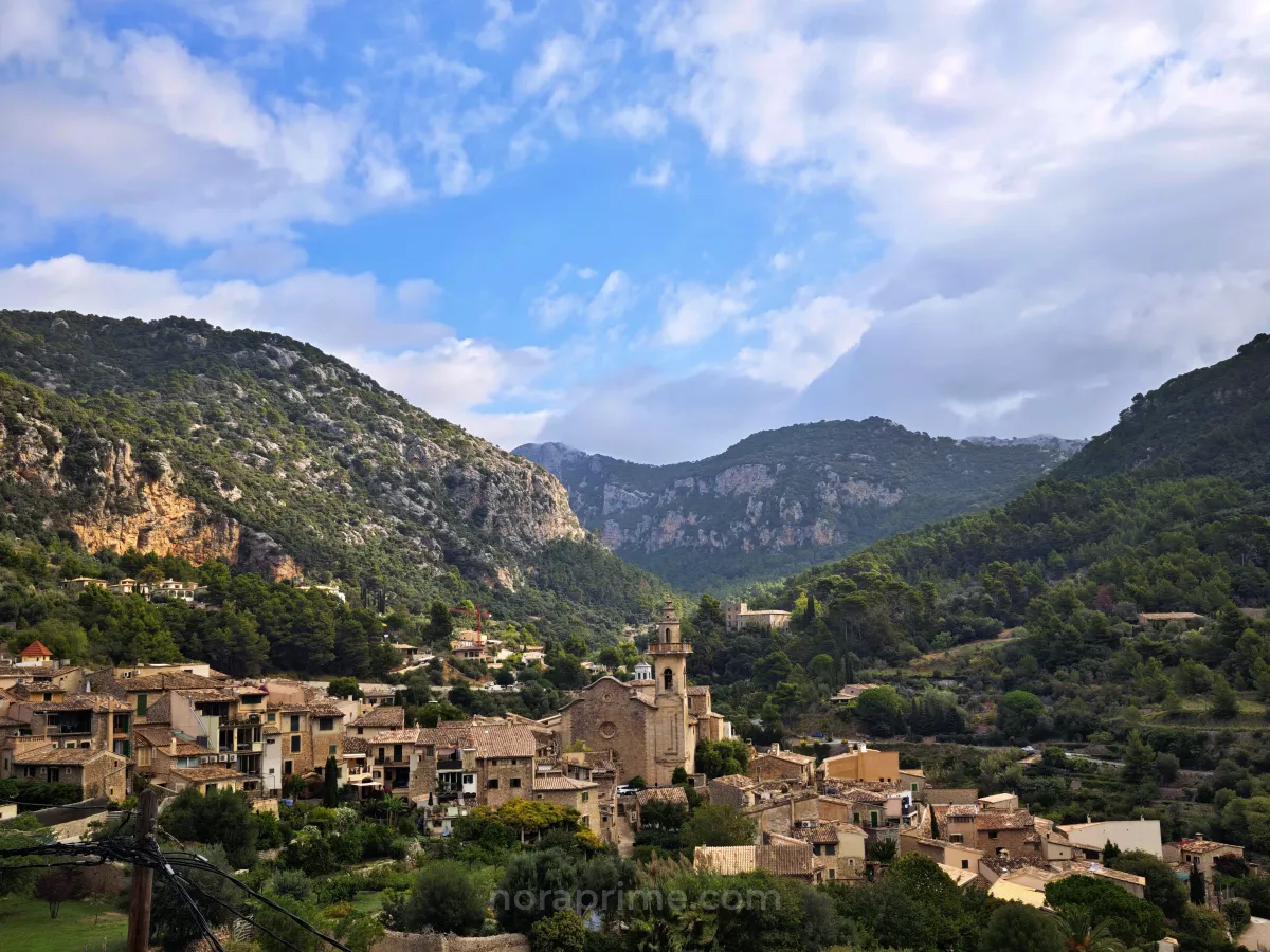 Vista general del pueblo de Valldemossa en Mallorca, con tejados de teja, campanario y montañas de la Serra de Tramuntana rodeando el valle.